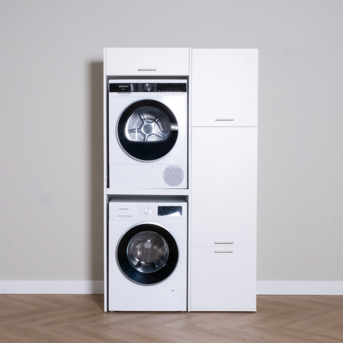 White stacked washer and dryer set next to tall white storage cabinet on wood floor.