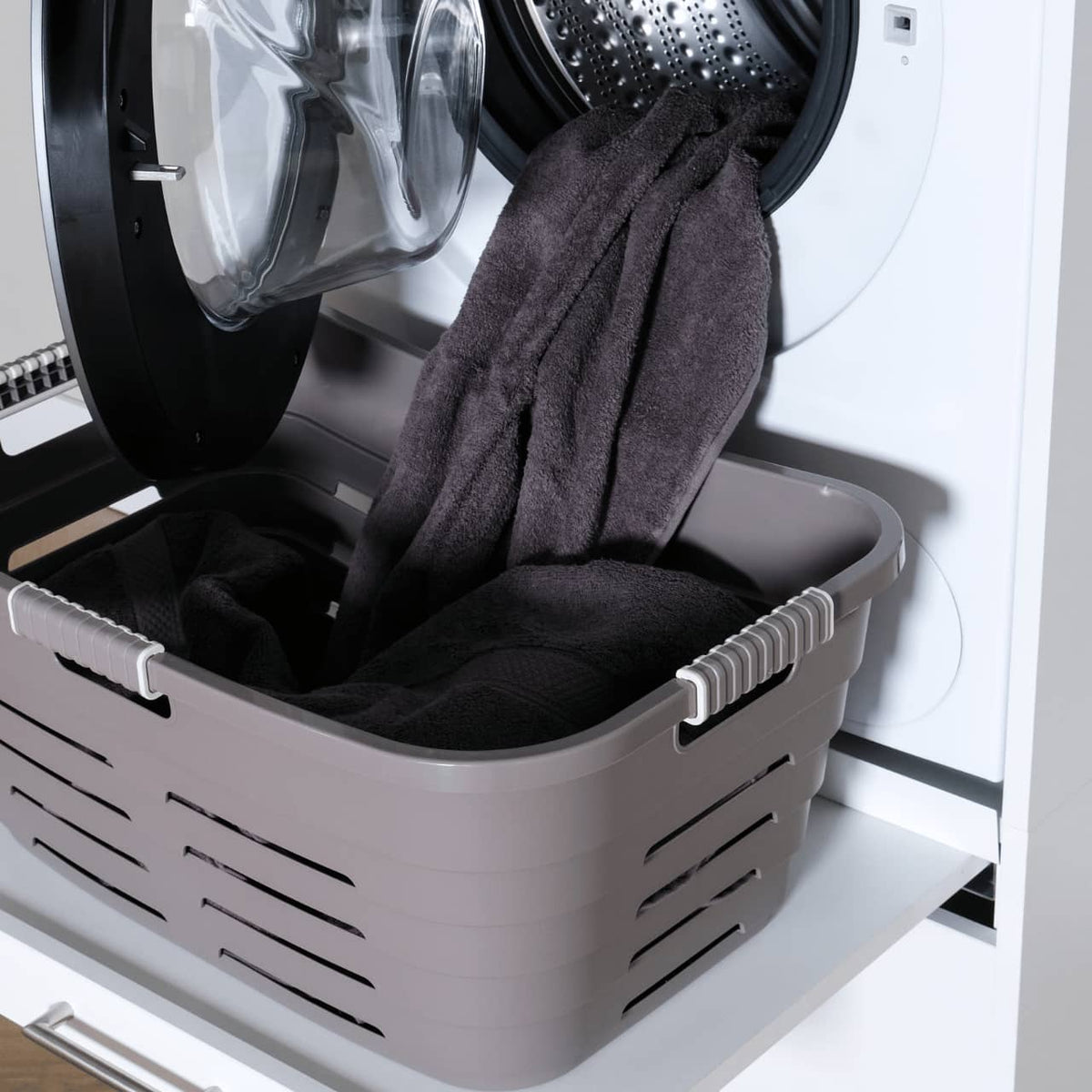 White plastic laundry basket with black towels in front-loading white washing machine.