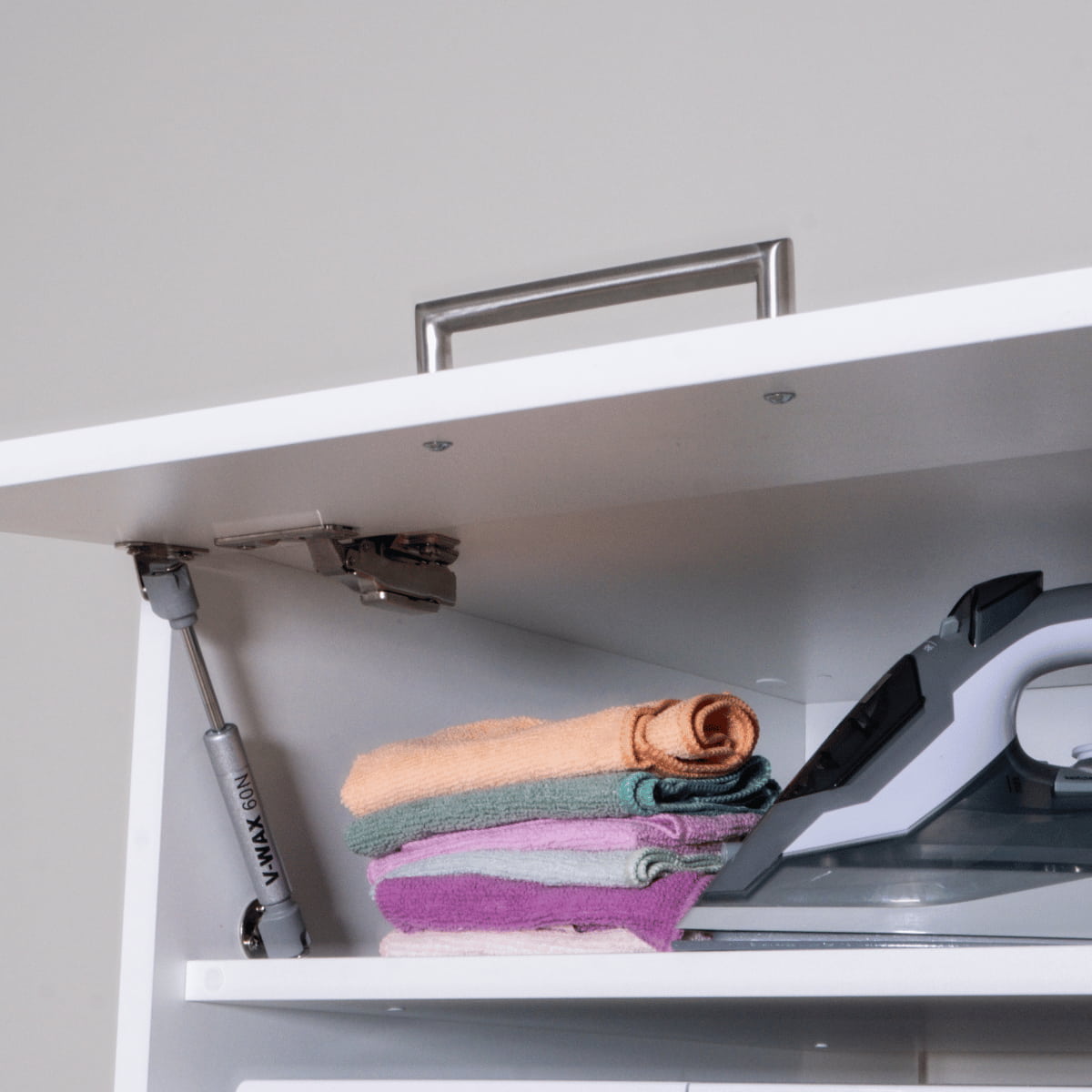 White cabinet interior with three folded pastel towels and a modern iron on the right side.