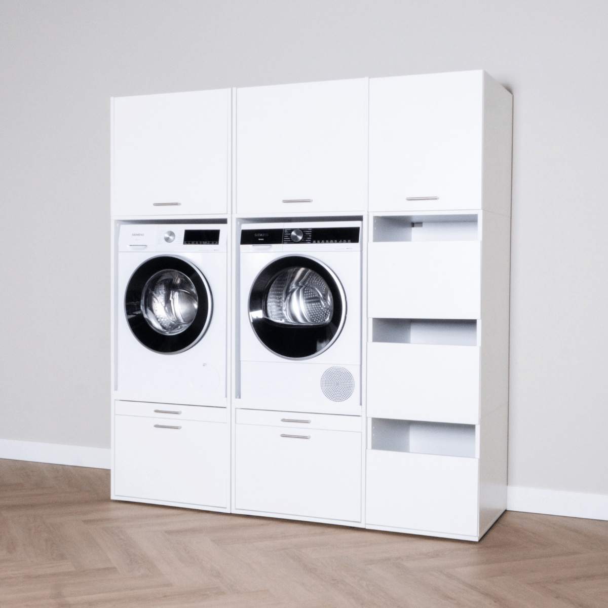 White laundry cabinet set with front-load washer, dryer, and open shelving unit on wood floor.