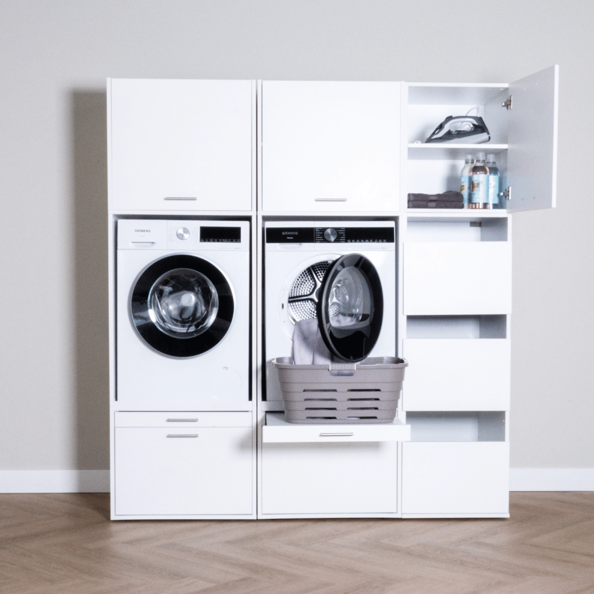 White modern laundry storage unit with front-load washer and dryer, open dryer door with laundry basket, and upper shelves.